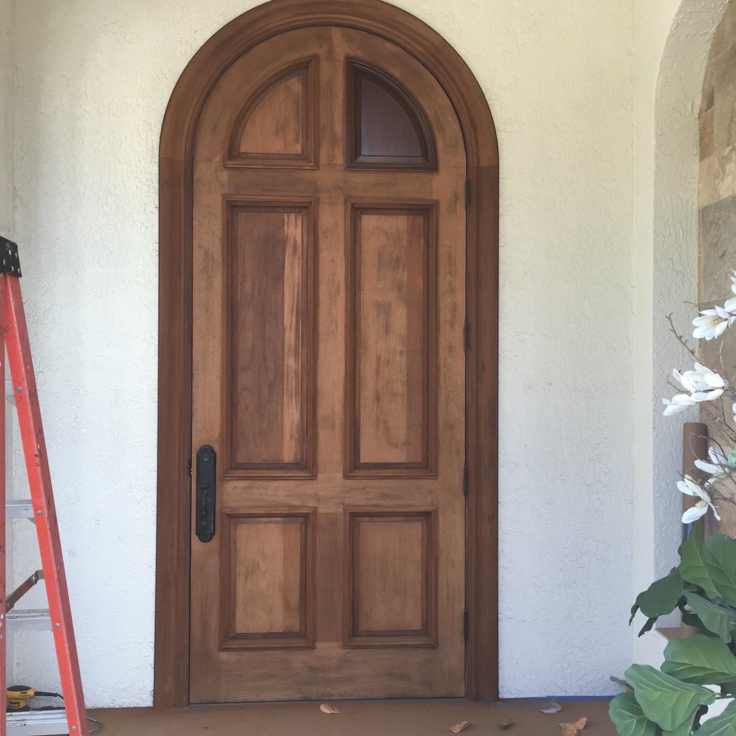 Arched wood entry door mid-refinishing with first stain coat applied